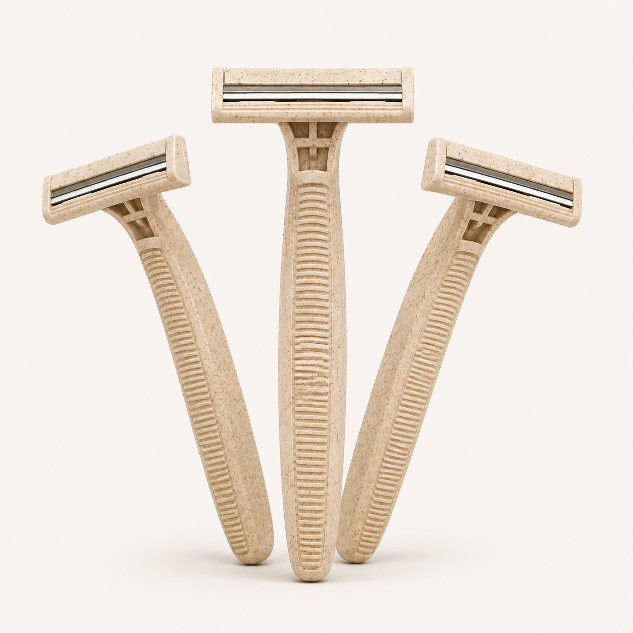 Trois rasoirs jetables biodégradables à deux lames avec longs manches texturés en paille de blé beige.